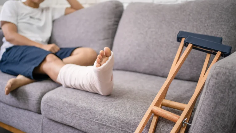 person with leg in cast sitting on couch, crutches nearby